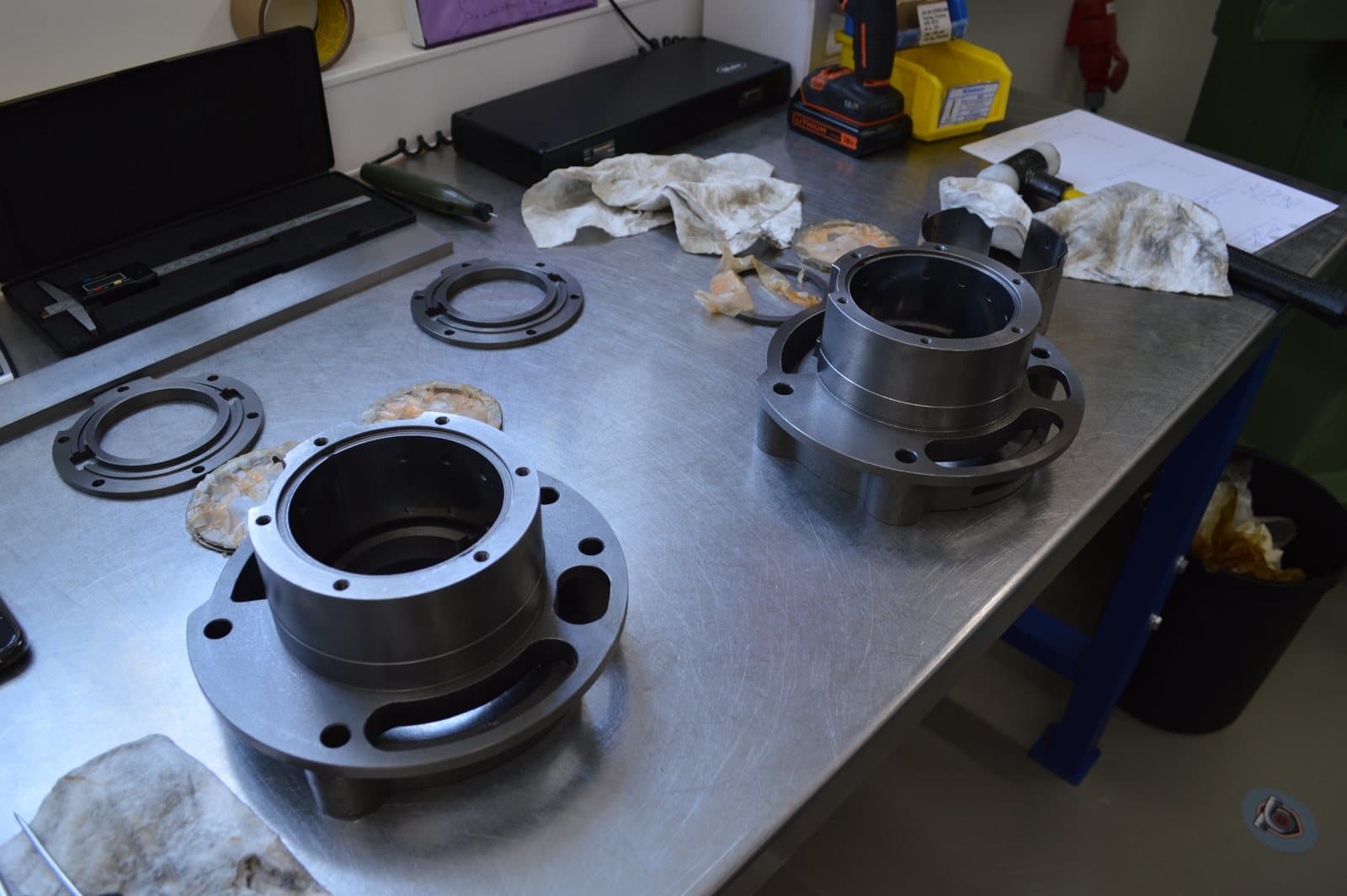 Two machined turbocharger bearing housings and their seal rings laid out on a steel bench