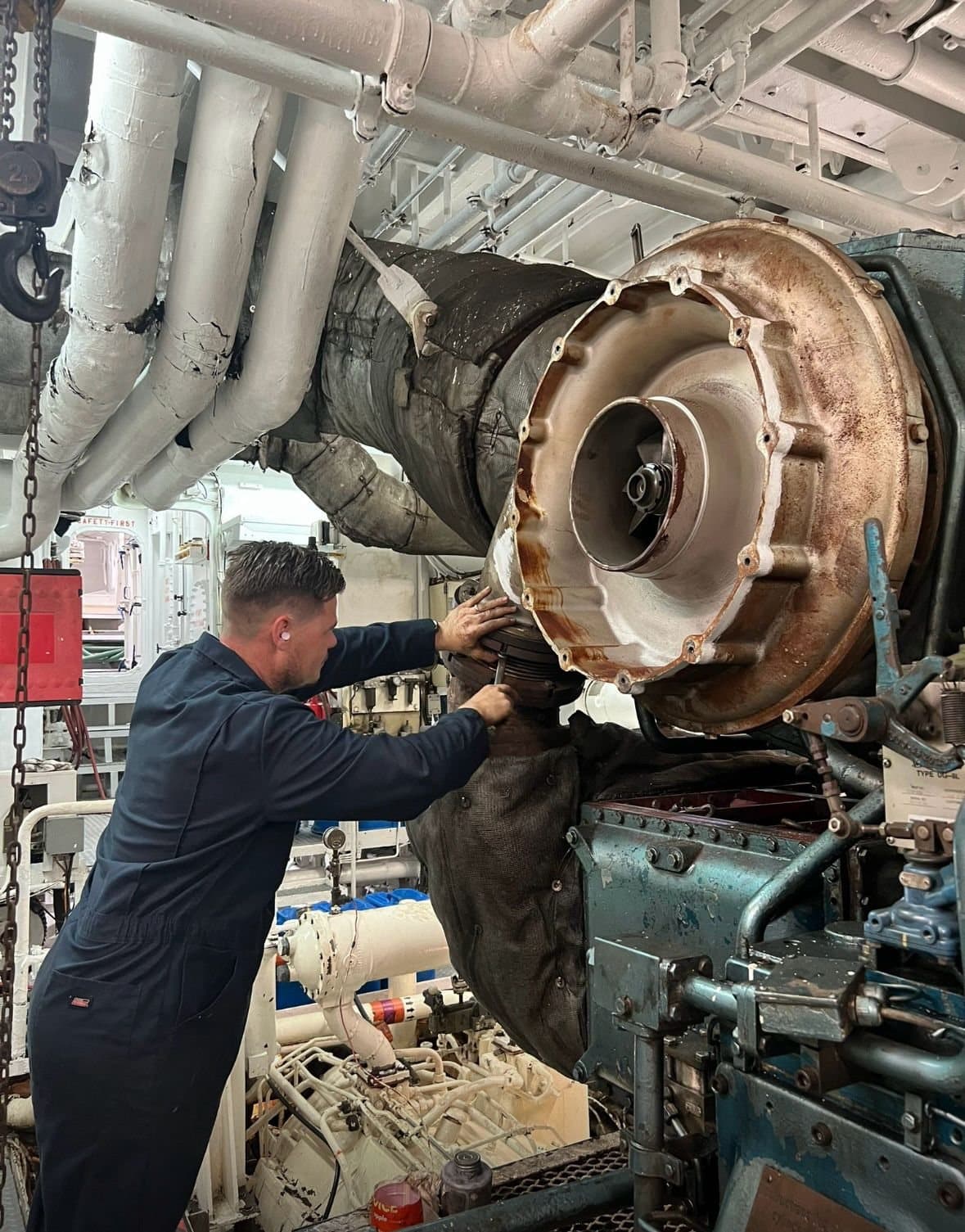 Engineer servicing a turbocharger mounted on a marine engine in an engine room