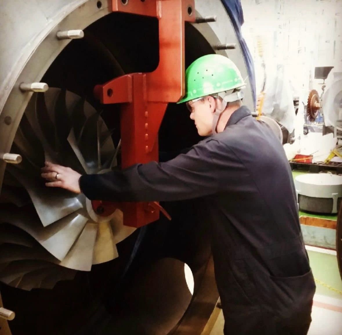 Engineer in a green helmet checking the turbine blades of a large marine turbocharger